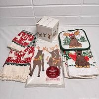 Photo of vintage reindeer tablecloth in its unopened package, a box with reindeer mugs, and reindeer-themed kitchen linens including potholders and towels.