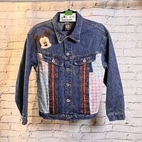 Front view of the denim jacket showing embroidered Mickey Mouse face and decorative patterned fabric patches on front.