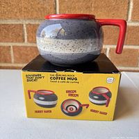 Photo of the curling stone shaped coffee mug displayed on top of its original yellow box with brand and product information.