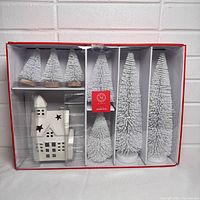 Photo of boxed set showing 7 snowy trees and white ceramic church in separate compartments of box.