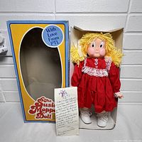 Open box showing Susie Moppet doll in red dress with lace, yellow yarn hair, white shoes, and handwritten note included