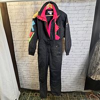 Front view of black vintage Obermeyer women's ski suit with colorful geometric accents and front zipper/button closure.