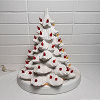 White ceramic Christmas tree on flat oval white ceramic base with red and yellow bulbs, unlit.