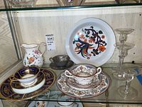 Minton Hazelmere marked plate, soup cup and saucer, Minton plate and teacup, handpainted Orion teacup with saucer, Royal Worcester Imari bowl, Wedgwood pitcher, three glass candleholders arranged on glass shelf.