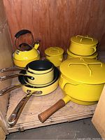 Overview of yellow cookware grouped inside cabinet showing nested Circulon pots, Dansk lidded casseroles and kettle