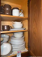 Cupboard shelves with stacked bowls, mugs, and plates in Denby stoneware in brown and beige tones.