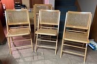 Four folding chairs arranged in a row showing front views of the cane seats and backrests with beech wood frames.
