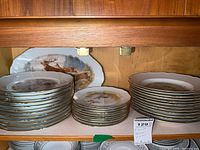 Wide shot showing stacked dinner plates, salad plates, and dessert plates with wildlife and nature designs inside wooden cabinet.