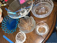 Top-down view of six glass and crystal bowls including a large clear bowl on a wooden base and a vibrant blue bowl with open lattice rim.