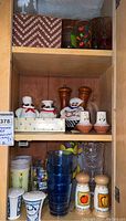 Cabinet shelf showing various tumblers, salt and pepper shakers, and taller drinking glasses including wooden pepper mills and ceramic shakers.