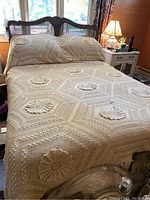 Full view of the antique hand crocheted full bedspread on a bed with matching pillow shams in a warmly lit bedroom.