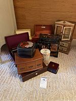 Assorted jewelry and keepsake boxes grouped on carpet including wooden, lacquer, and a tall floral cylindrical box.