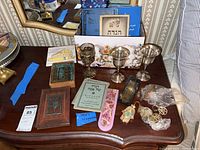 Overview of table showing 3 Kiddush goblets, leather-bound books, Haggadah booklets, mezuzahs, keychains and other small Judaica items.