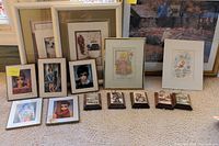Lot showing multiple framed and unframed art prints, mainly of children with large eyes in Keane style, along with winter scene prints in small wooden frames lying on carpet.