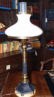 Full view of metal table lamp with white glass globe shade and bookshelves in the background.
