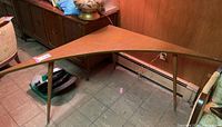 Side view of vintage corner table showing triangular wooden top with gold-tone metal legs and scratches.