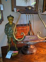 Side view of Le Siffluer boy figurine next to the wooden music stand with brass rods and decorative carved floral motifs