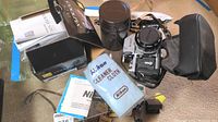 Wide view showing film camera with attached lens in leather case, cleaning cloth, strap, Coolpix S230 box and manuals