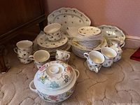 Overall lot arranged on floor showing stacks of plates, cups, saucers, tureen, creamer and platter