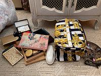 Overview of vintage compacts, makeup bags, travel cosmetic bag and assorted items displayed on carpet in front of white painted furniture.