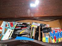 Wooden drawer interior with assorted pens, markers, and ink tubes
