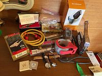 Overview of assorted lot items on table including ornament box, pen case, cord, steamer box, tape dispenser, tools, watch parts tin and small hardware
