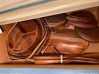 Wood sectioned serving bowls and baskets arranged inside a cabinet, showing multiple items of different shapes and sizes including oval and round pieces.