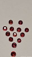 Multiple round faceted sapphires laid out on white background showing fire red to orange hues and reflective facets.