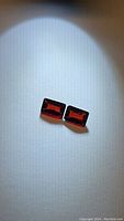 Photo of a pair of rectangular deep red octagon cut almandine garnet gemstones on a white background.