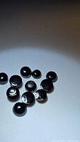 Group of 11 round black onyx cabochon gemstones laid on white background showing smooth, polished domed surfaces.
