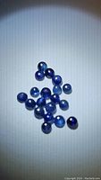 Group of small round and oval blue sapphire cabochons arranged on white surface, showing their deep blue color and smooth polished dome shape.