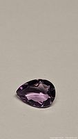 Front angle photo of the pear-shaped purple amethyst gemstone on a neutral background showing cut and clarity.