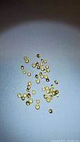 Top-down photo showing multiple small round yellow sapphires scattered on a white surface, bright and clear stones visible.