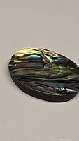Close-up photo of oval abalone doublet gemstone showing intricate natural iridescent pattern and color variations in green, blue, and brown on polished surface.