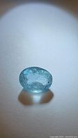 Clear well-lit close-up of an oval aquamarine gemstone showing facets and light blue color, placed on a white background.