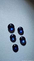 Five round cabochon blue sapphire gemstones on a light background showing their smooth, domed shape and deep blue color under direct light.