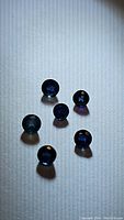Top view of six natural blue sapphires arranged loosely on a white surface, showing size and deep blue color.