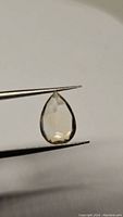 Photo of pear-shaped natural golden citrine gemstone held with tweezers showing transparency and yellow color.