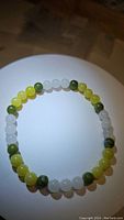 Clear photo of circular elastic bracelet made from alternating 6mm jade beads in green, yellow, and white colors, placed on illuminated white surface.