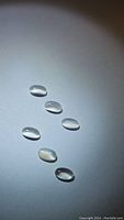 Six oval cabochon white moonstones arranged under light showing translucency and adularescence.