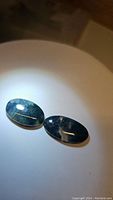 Two oval dark green moss agate cabochons under lighting showing natural inclusions and glossy polish.