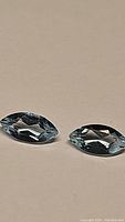 Close-up photo of two marquis cut natural sky blue topaz gemstones placed next to each other on a neutral background, showing clarity and color.