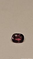 Close-up photo of the natural intense pink spinel gemstone showing cushion cut and rich pink color on a neutral background.