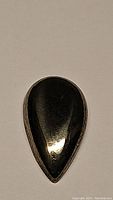 Close-up photo of the pear-shaped pyrite cabochon showing its smooth polished surface and metallic gold-silver color.