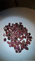 Photo of natural rough garnet crystals on a white plate showing their reddish to pinkish orange color and rough texture