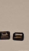 Pair of rectangular emerald cut smokey quartz stones placed on a solid neutral background to showcase clarity, cut, and color.