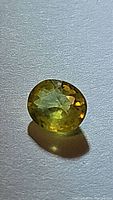 Close-up photograph of a polished oval yellow sapphire gemstone on a white surface showing canary yellow color and internal clarity.