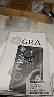 Ring placed on GRA certification card showing certification details including size 8.0mm, 2.0ct weight, D color moissanite gemstone.