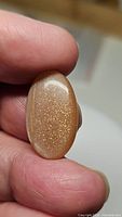 Photo of an oval cabochon cut peach moonstone showing sparkling internal inclusions held between fingers.