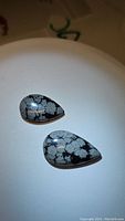 Two pear-shaped cabochon snowflake obsidian stones displaying distinct gray snowflake-like patterns on glossy black surface.